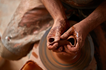 Close-up hands of a male potter in apron squizing wrong bowl from clay, selective focus
