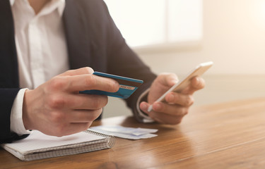 Man's hands holding a credit card and using smartphone
