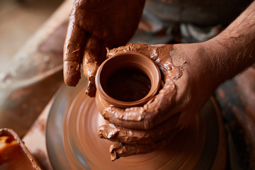 Close-up hands of a male potter in apron molds bowl from clay, selective focus