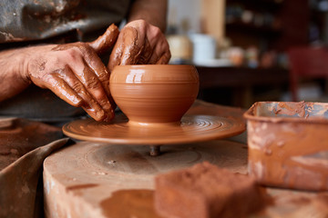 Fototapeta na wymiar Close-up hands of a male potter in apron molds bowl from clay, selective focus