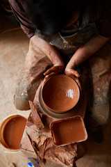 A male potter in apron molds bowl from clay, selective focus, close-up