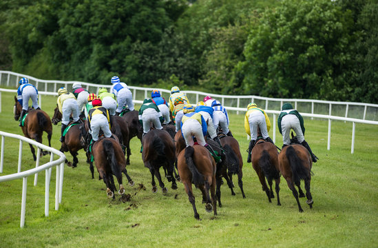 View from behind of galloping race hoses and jockeys going down the race track