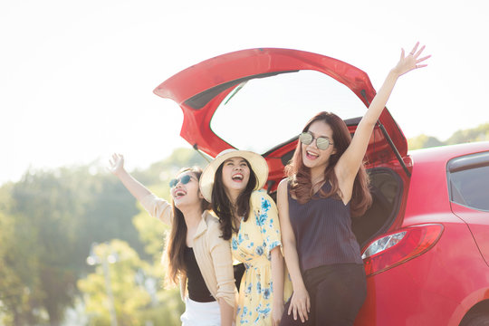 Enjoying woman with her girlfriend traveler sitting on hatchback red car. summer vacation, holidays, travel, road trip and people concept .