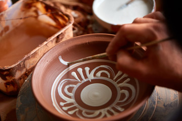A potter paints a clay plate in a white in the workshop, top view, close-up, selective focus.