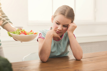 Woman offering her daughter salad but girl refusing