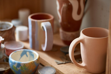 Handmade potter mugs and paint bowl on a wooden shelf, close-up, shellow depth of field.