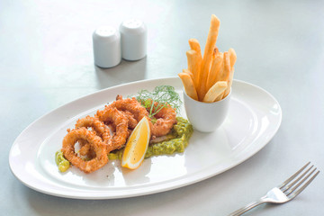 crispy calamari rings,deep fried calamari with sauce,lemon and french fries on white plate