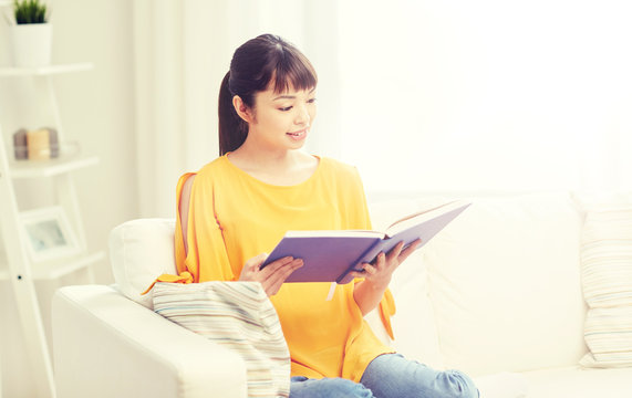 leisure, literature and people concept - smiling young asian woman reading book at home