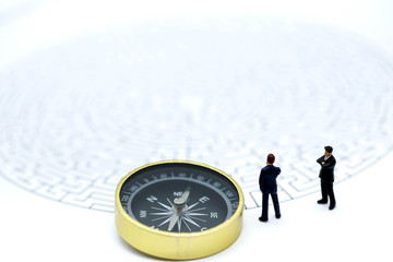 Miniature people: Businessman standing on start point of maze with compass , businessman making the right choice concept.