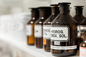 Close-up of the labeled glass container of a chemical pharmaceutical substance on a shelf, next to various supplies in the storage of a modern drugstore