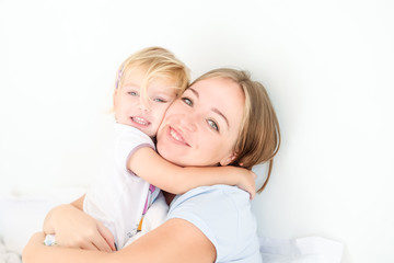 Portraits of Happy and loving mother embracing her daughter on the bed. Family morning concept. Spending free time together at home. Soft selective focus. Space for text.