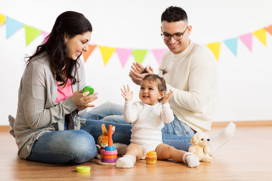 family, holidays and people concept - happy mother, father and little daughter with toys playing and clapping hands on birthday party