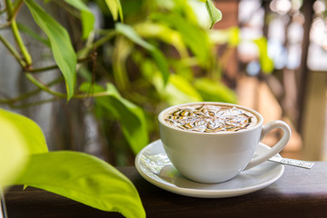 Latte art coffee cup with blur of plants on wood