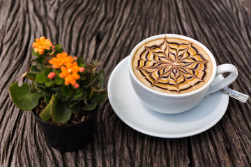 Latte art coffee cup with flowers vase on texture wooden table
