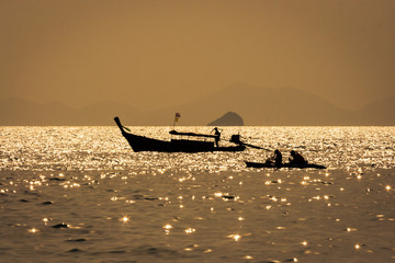 Obraz premium Thai long boat and a kayak at sea at sunset, with golden colors, in Railay beach, Krabi, Thailand.