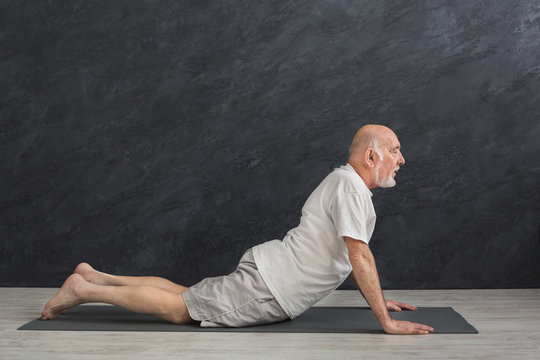 Senior man training yoga in cobra pose indoors
