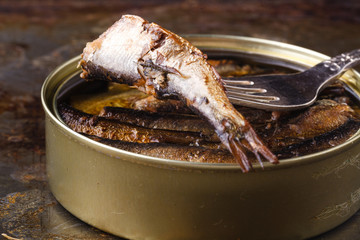 Open canned fish near fork on rustic background