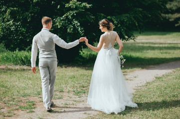 Stylish couple of happy newlyweds posing in the park on their wedding day