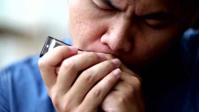 South east asian men playing music with harmonica in close up