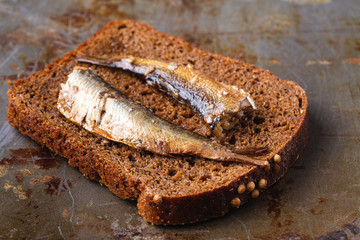 Canned sprats in tin can with rye bread. On rustic background