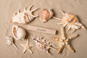Fototapeta na wymiar The inscription June on sand with starfish and seashells