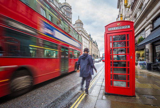 London, England - Iconic blurred red double-decker bus on the move with traditional red telephone box and walking man in the center of London at daytime
