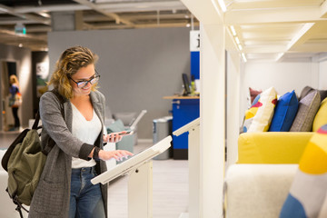 Woman with phone configuring furniture at the self-service device in the store