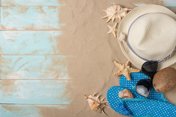 Fototapeta na wymiar Hat, sunglasses, slippers with shells and coconut and sand on a wooden background, top view with empty space