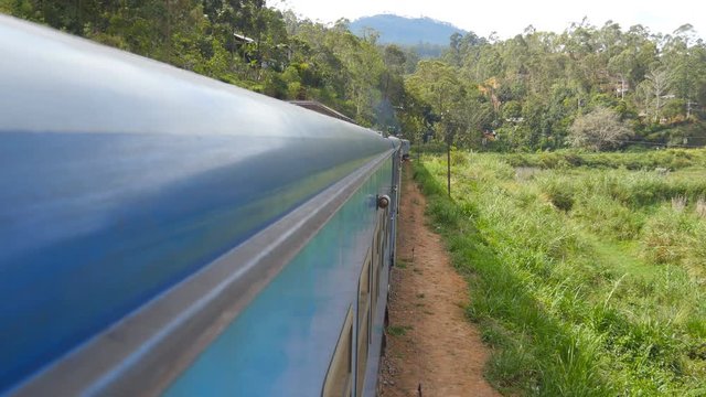View from window of old blue train moving in scenic countryside at sunny day. Passenger railway transport riding through beautiful nature landscape. Concept of travel. Close up
