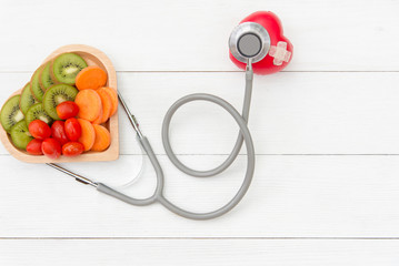 Diet and weight loss for healthy care with medical stethoscope, vegetable fruit and healthy food with red heart on the old white wooden background top view. Healthy Concept.