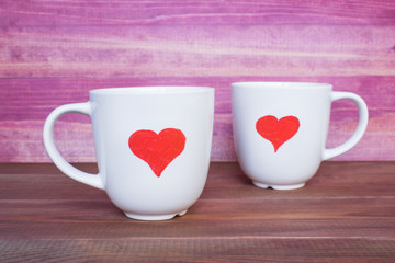 Two white mugs with drawn hearts on the pink background, love concept.