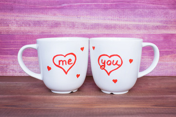 Two white mugs with drawn hearts on the pink background, love concept.