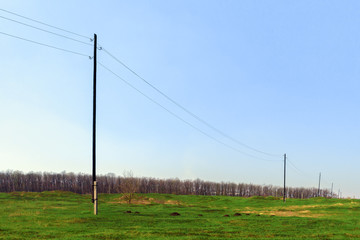 Power line with wooden poles and concrete base on a green field in the spring.