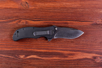 Folding knife with black handle on wooden backgound