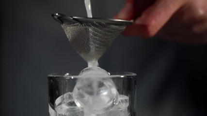 Bartender straining white liquid in an ice filled transparent glass