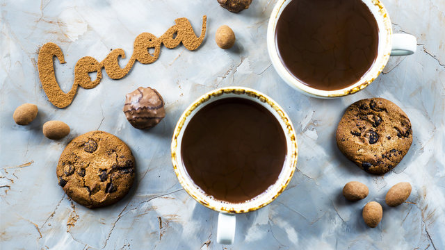 Fototapeta The word cocoa is written in letters of cocoa on a gray concrete background next to two cups of cocoa and chocolate sweets and biscuits. I love the cocoa concept