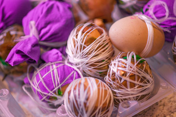 Obraz na płótnie Canvas Easter eggs prepared for dyeing in onions peels, decorated with natural fresh leaves, plants, rice, colorful fabric and tied with white threads. Eggs laying in wicker wooden basket full of green grass