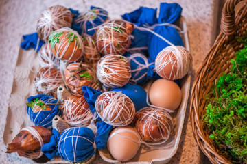 Easter eggs prepared for dyeing in onions peels, decorated with natural fresh leaves, plants, rice, colorful fabric and tied with white threads. Eggs laying in wicker wooden basket full of green grass
