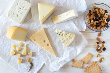Different kinds of delicious cheese with nuts and herbs on white table.