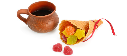 Coffee cup and marmalade candies in a waffle horn isolated on white . Wide photo.
