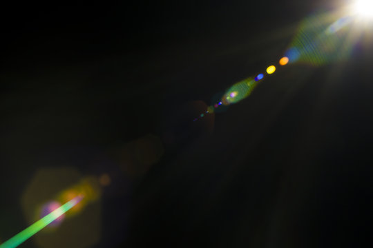 Solar camera lens flare light create hexagon of objective iris shapes of different colors depending on used antireflection coating of each lens surface on dark black background - Powered by Adobe