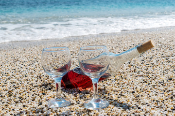 Bottle of red wine with wine glasses on the beach at the summer sunny day. Sea on the background.