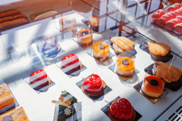 Assortment of cakes on cafe showcase. Variety of flavours. Chocolate and cream cakes in store with fruits and jelly.