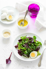 Fresh salad with beetroot, mix leaves, olive oil, egg and sesame seeds on white table cloth