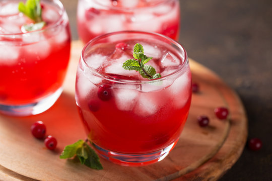 Summer cold beverage with cranberry, ice cubes, mint on the wooden cutting board.