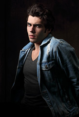 Thinking serious charismatic man in blue jeans looking on dark shadow dramatic light background. Closeup portrait. Art