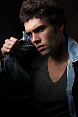 Sexy serious angry male model posing in blue jacket on dark shadow background. Fashion style contrast vogue portrait