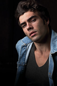 Sexy Serious Male Model Posing In Blue Jacket On Dark Shadow Background. Fashion Style Contrast Vogue Portrait