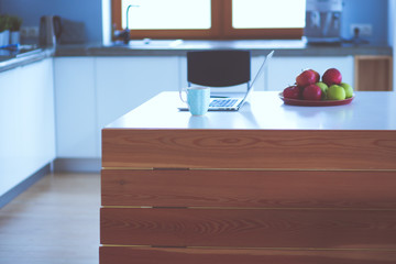 Young woman sits at the kitchen table using a laptop and talking on a cell phone.