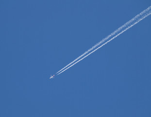 commercial plane furrowing the blue sky with two jets of smoke